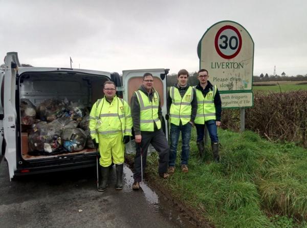 four people in high vis jackets outside the sign for liverton village